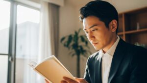 朝の光の中で読書に集中するスーツ姿の男性。朝活はメリットだらけと言われるように、始業前の時間を有効活用して充実した一日をスタートさせている様子。