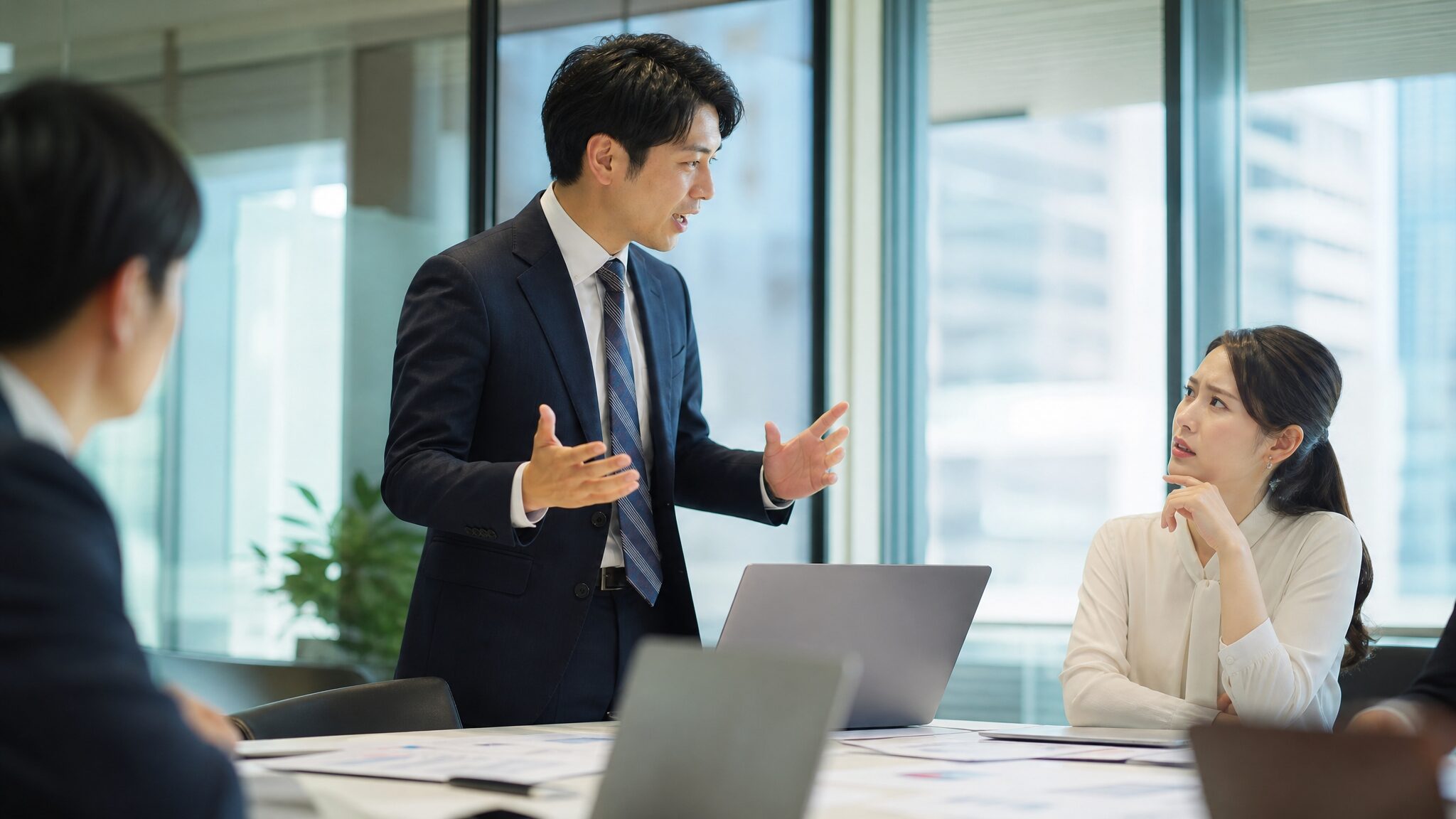 会議室で熱弁する男性社員の話を困惑気味に聞く女性社員の様子で、横文字を使いたがる人の心理を象徴するシーン。